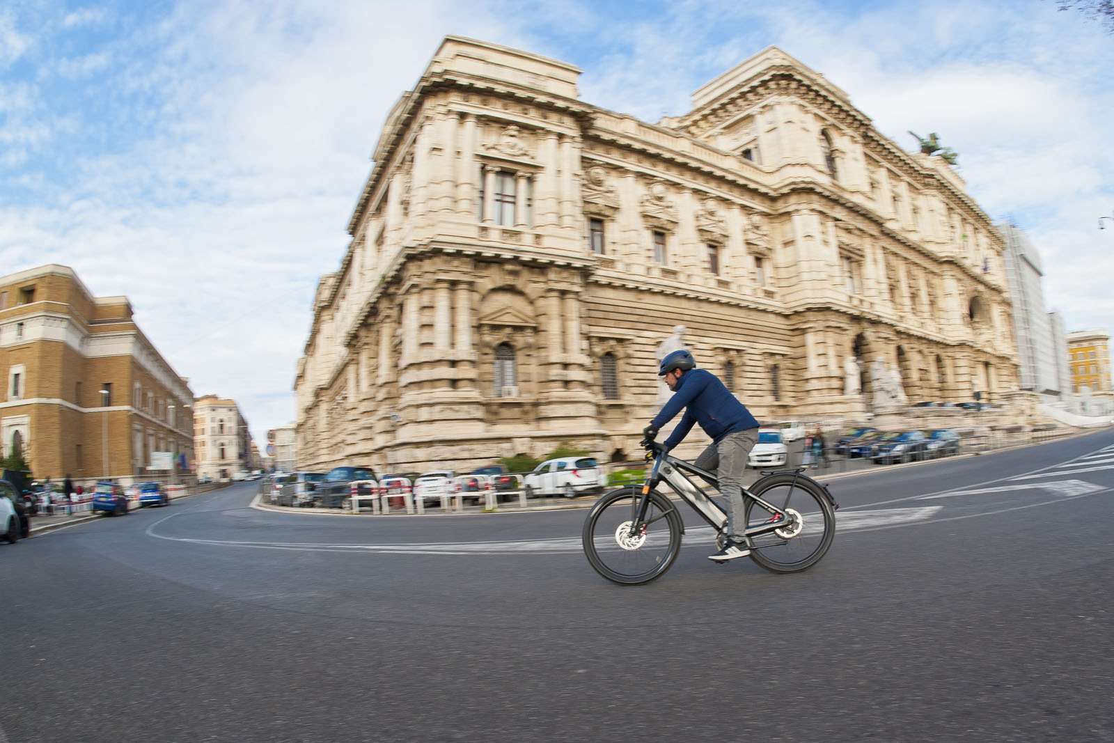 Ciclista in e-bike su una strada cittadina davanti a un palazzo storico